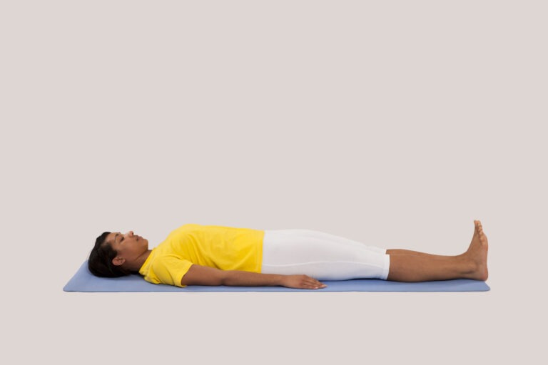 Lying on your back with legs together and arms next to the body, palms facing downward